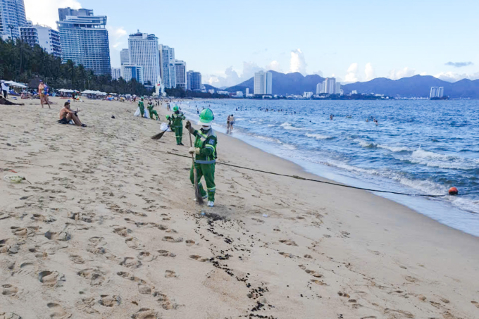 Nhân viên môi trường thu dọn dầu vón cục trên bãi biển Nha Trang. Ảnh: Hải Vân